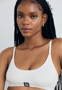 Hvit ribbet bralette med tynne stropper og et logo-merke. Glatt stoff med minimalistisk design, med en scoop-halsutskjæring og en tettsittende passform.