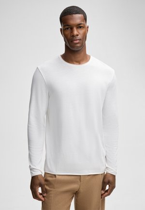 weißes Langarmhemd aus leichtem Stoff, mit Rundhalsausschnitt und glatter Textur, kombiniert mit beigen Hosen.