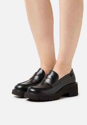 Mustat nahkaiset loafersit, joissa on paksu korokepohja, hienovaraiset saumat ja tyylikäs muotoilu. Minimalistinen tyyli ja sileä pinta.