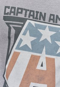 Šedé bavlněné tričko s odvážnou grafikou štítu a hvězd, s nápisem "Captain America" v tmavém písmu. Opotřebovaný vzhled po celém povrchu.