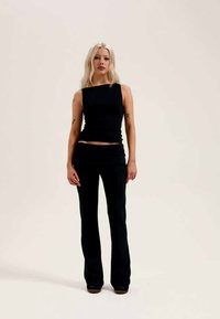 Juodas prigludęs marškinėlių topas su kvadratiniu iškirpimu, derinamas su aukštu juosmeniu flared kelnėmis. Lygus audinys su minimaliais puošmenomis, sukuriantis elegantišką siluetą.