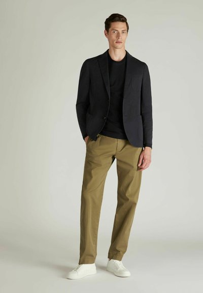 Navy Blazer mit Revers über einem schwarzen T-Shirt, kombiniert mit olivfarbenen Chinos und weißen Sneakers. Glattes Material und taillierte Passform.
