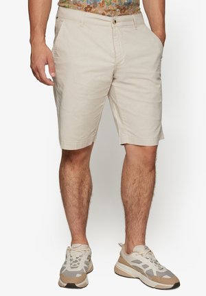 Beige bomulds shorts med lige snit, to sidelommer og opsmøgede kanter. Kombineret med beige og taupe træningssko.