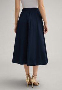 Marineblaues Midikleid mit elastischem Bund. Weicher, leichter Stoff; ausgestellte Form. Kombiniert mit goldenen High-Heels.