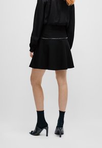 Zwarte uitlopende rok met een strakke tailleband met zilveren studs. Gemaakt van zachte stof, valt boven de halve bovenbeenlengte.