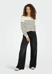 Gestreepte crèmekleurige trui met rode hartaccenten, gecombineerd met zwarte wijde broek. De trui heeft lange mouwen en een relaxte fit.
