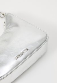 Metalen zilveren handtas met een zachte textuur, hoekige vorm en een ritssluiting. Bevat een logo in een verhoogde zilveren metalen afwerking.
