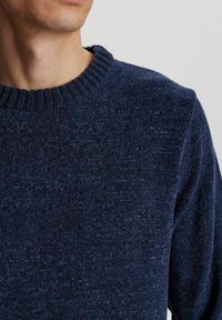 Marineblau gestrickter Pullover mit einem gerippten Rundhalsausschnitt. Die Textur wirkt weich und leicht fusselig und zeigt ein einheitliches, gleichmäßiges Muster.