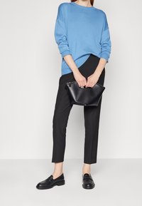 Helles blaues, übergroßes Strickpullover mit überschnittenen Schultern; schwarze, tailored Hosen; schwarze Leder-Clutch; schwarze Loafer mit glatter Oberfläche.