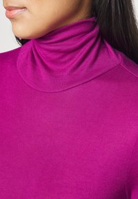 Dopasowany golf z żywej fioletowej dzianiny. Gładka faktura z wysokim kołnierzem, prezentująca bezszwową sylwetkę.