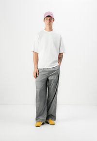 Bílý krátký rukáv tričko, šedé volné kalhoty a žlutá obuv. Růžová čepice dotváří outfit. Jednoduchý design bez výrazných vzorů.