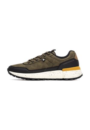 Zapatillas de ante verde con detalles en negro, media suela blanca con manchas y un detalle amarillo en el talón. Presenta seis ojetes y una suela texturizada.