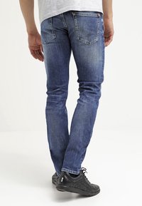 Jeans de mezclilla azul con corte ajustado, lavado desgastado y sutiles arrugas. Presentan dos bolsillos traseros con un diseño decorativo de costuras.