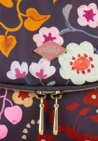 Floraal bedrukte stoffen tas in donkerpaars, met heldere roze, oranje en witte bloemen. Gouden logo label en ritshardware accentueren het ontwerp.