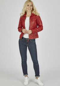 Rote Lederjacke mit Reißverschluss-Taschen, getragen über einem weißen Hemd. Kombiniert mit dunklen Jeans und weißen Sneakern. Glatte Textur, taillierte Passform.