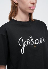 T-shirt nera con logo "Jordan" in strass bianchi e dettagli dorati, collo rotondo e maniche corte. Tessuto di trama liscia.