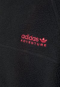 Černý fleecový pulover s logem "adidas ADVENTURE" v červené výšivce, hladkou texturou a vysokým límcem.