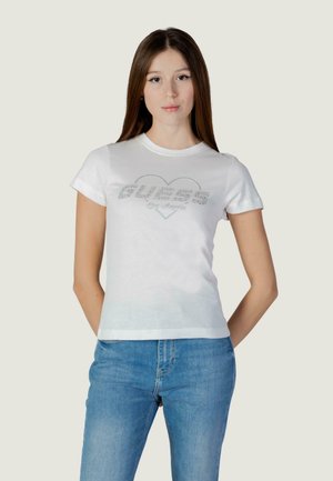 T-shirt bianca a maniche corte con un motivo a forma di cuore e la scritta "GUESS Los Angeles" in lettere argentate scintillanti sul davanti.