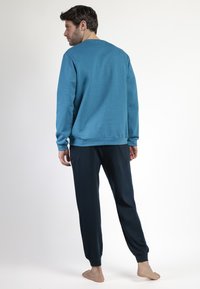 Sudadera azul de manga larga, cuello redondo y puños acanalados, combinada con pantalones de chándal azul oscuro que cuentan con tobillos elásticos.