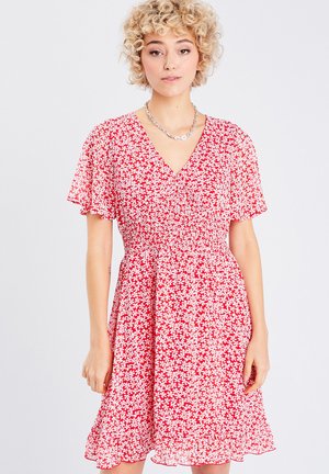Robe florale rouge avec de courtes manches volantées, décolleté en V, taille smockée et ourlet à volants, ornée de petits motifs de fleurs blanches.