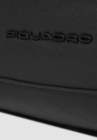 Zwarte leren tas met het geperste "Piquadro"-logo, gladde structuur en subtiele stikseldetails. Compact rechthoekig ontwerp.