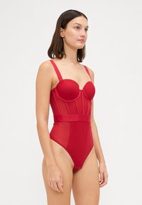 Roter Einteiler-Badeanzug mit vorgeformten Cups, durchsichtigen Einsätzen und einem breiten Bund. Verfügt über verstellbare Schulterträger und hohe Beinausschnitte.