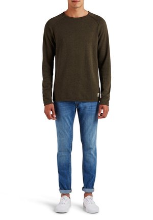 Olijfgroene langemouwshirt met een ronde hals en raglanmouwen, gecombineerd met lichtblauwe jeans en witte sneakers, rechtopstaand.