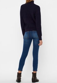 Laivastonsininen neulepaita, jossa korkea kaulus, yhdistetty sinisiin slim fit -farkkuihin ja mustiin nilkkureihin. Sileä rakenne ja vartalonmyötäinen malli.