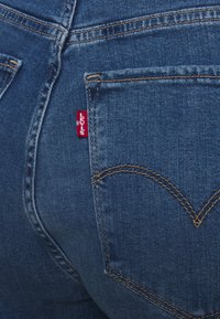Un jean en denim bleu présente une étiquette rouge Levi's sur la poche arrière. La couture est d'un jaune contrastant, avec un design de poche courbe classique.