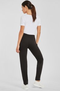 Schwarze Sporthosen mit einem dehnbaren Bund, schmaler Schnitt und Seitentaschen, kombiniert mit einem schlichten weißen T-Shirt und leichten Turnschuhen.