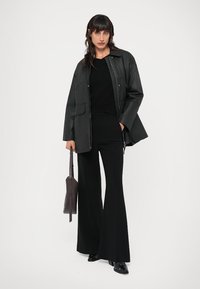 Casaco de couro preto com um corte relaxado, combinado com um suéter preto ajustado e calças pretas largas. Os acessórios incluem uma bolsa escura.