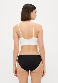 Bralette alb cu dungă, cu bretele ajustabile, asortat cu chiloți negri din bumbac. Linii curate, design fără cusături și o siluetă ajustată.