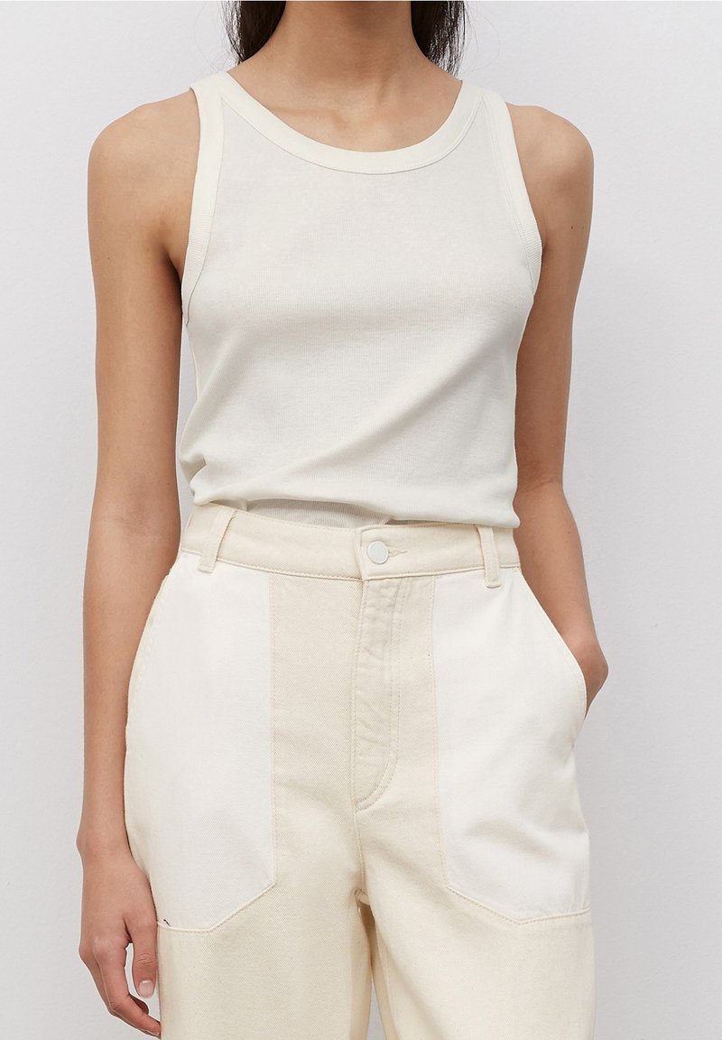 Top senza maniche beige chiaro con texture a costine e scollatura ampia, abbinato a pantaloni crema a vita alta con tasche a toppa.