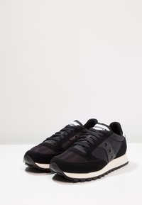 Czarne buty sportowe wykonane z połączenia materiałów siateczkowych i zamszowych, charakteryzujące się teksturowaną powierzchnią, sznurowanym zapięciem oraz białą podeszwą środkową.