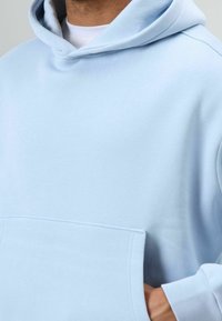 Sweat à capuche bleu clair avec une texture douce, doté d'une grande poche frontale, d'une capuche à cordon de serrage et de poignets côtelés.