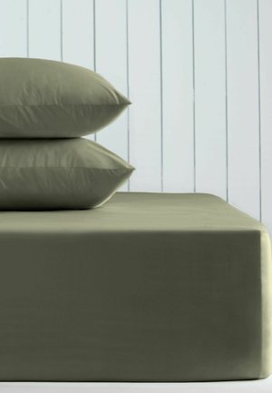 Zwei olivgrüne Kissen sind auf einem Bett mit passendem Spannbetttuch vor einer weißen vertäfelten Wand gestapelt.