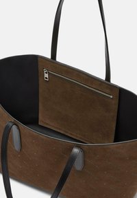 Borsa tote in suede marrone con dettagli in pelle nera. Presenta una tasca interna con zip e tessuto liscio e testurizzato con un sottile motivo del logo.