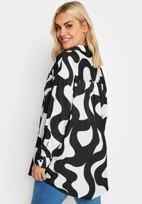 Camicia a maniche lunghe con un audace motivo astratto a spirale in bianco e nero, realizzata in tessuto morbido, con una vestibilità comoda e dettagli con bottoni.