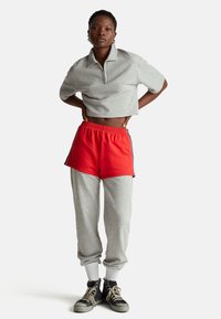 Šedé krátké polo s krátkými rukávy, doplněné červenými šortkami a šedými tepláky. Černé tenisky s bílými podešvemi. Jednoduchý, sportovní design.