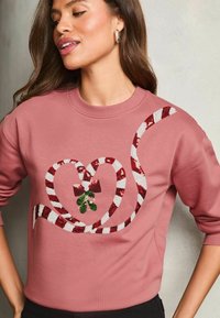 Sudadera rosa con un diseño de corazón hecho de bastones de caramelo rojos y blancos, adornada con muérdago verde y un lazo rojo.