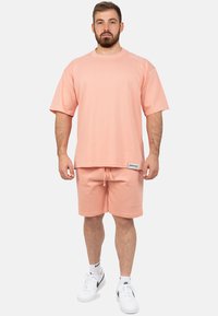 T-shirt a maniche corte di colore pesca con vestibilità comoda, abbinato a pantaloni corti coordinati con coulisse regolabile e branding discreto.