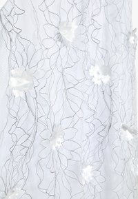 Bílá krajková látka s květinovou výšivkou a bílými aplikovanými květy. Jemné listové vzory v černé niti vytvářejí texturu a detaily.