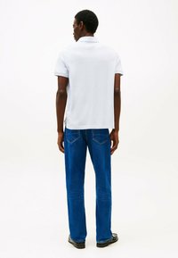 Polo shirt azzurro chiaro con colletto classico, abbinato a jeans blu scuro con tasche posteriori. Tessuto morbido e vestibilità casual.