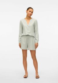 Lichtgroene linnen shorts set met een knoopsluiting in een V-hals top en shorts met trekkoord. Soepele textuur met een losse pasvorm en lange mouwen.