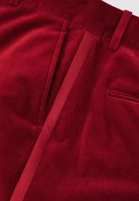 Röda sammetbyxor med en slät yta, skräddarsydd design, sidfickor och en kontrasterande innerfoder.