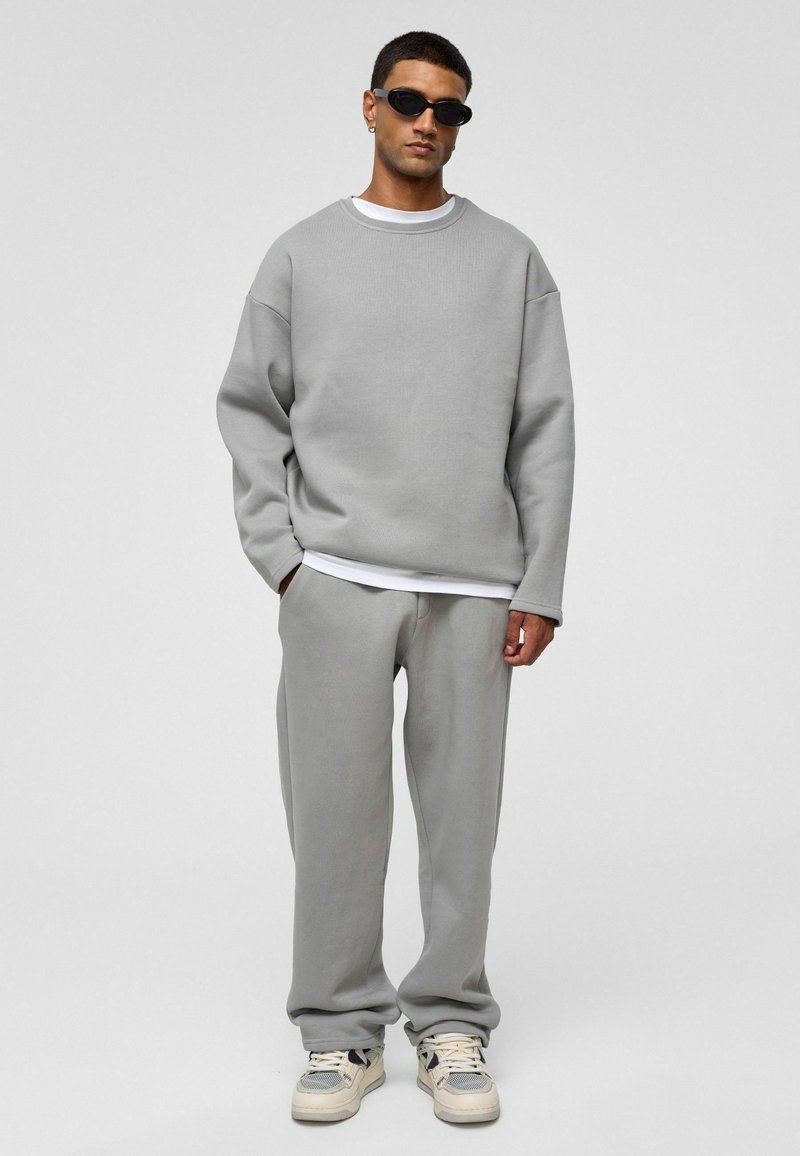 Grau Sweatshirt und passende Sweatpants mit entspannter Passform und gerippter Textur. Die Kombination mit einem weißen T-Shirt und Sneakern rundet den Look ab.