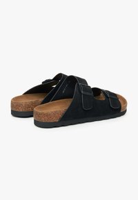 Zwarte suède slip-on sandalen met twee verstelbare banden, kurken voetbed en rubberen zool; heeft een bruine inlegzool en textuurdetails.