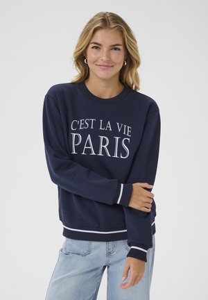 Sweatshirt bleu marine à manches longues, avec des poignets et un ourlet côtelés, arborant le texte blanc "C'EST LA VIE PARIS" à l'avant. Tissu en coton doux.