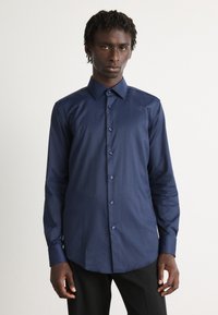 Camisa azul marino de botones hecha de una tela suave, con un cuello clásico, mangas largas y un dobladillo curvado con botones a juego.