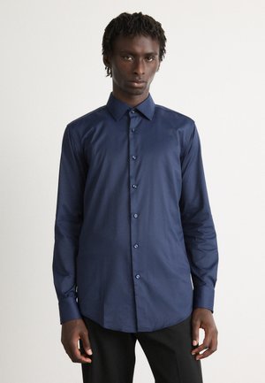 Camisa azul marino de botones hecha de una tela suave, con un cuello clásico, mangas largas y un dobladillo curvado con botones a juego.